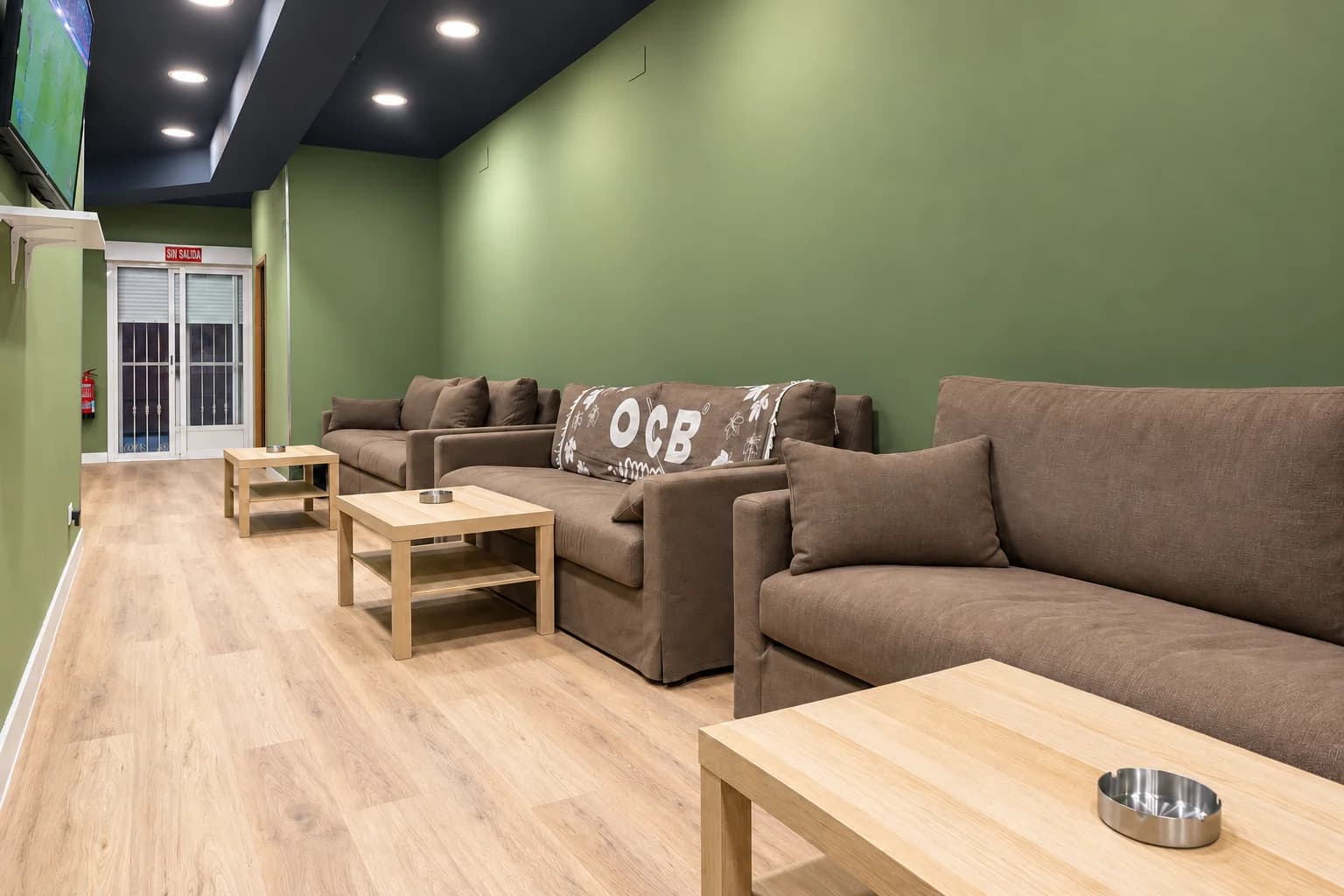 Weed Club Chueca lounge in Madrid with brown sofas, wooden tables and green walls