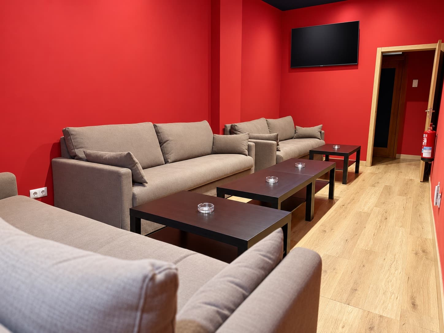 Lounge at Weed Club Gran Vía in Madrid with beige sofas, dark tables and red walls.